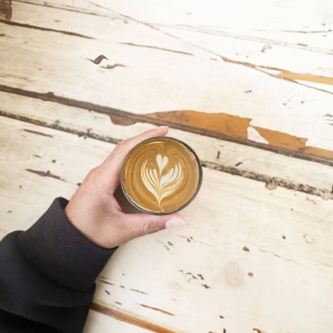 A cortado with tulip latte art held over Caffè D'Amore's vintage white-washed wooden table