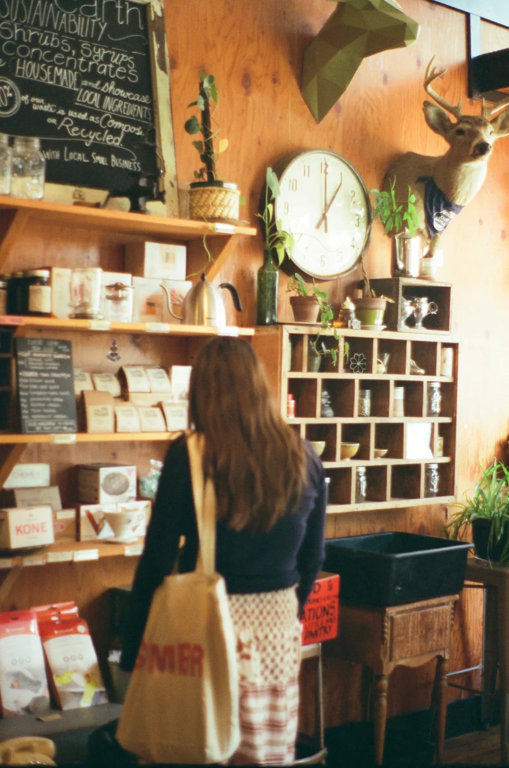 Guest browsing CDA's market shelves of coffee gear beneath the vintage wall clock