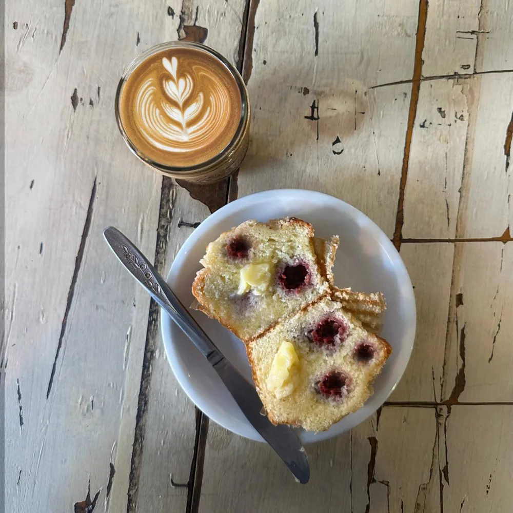 Mason jar latte with rosetta art beside a buttered raspberry muffin